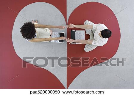 Man and woman sitting with laptops on large heart, arms out, touching hands, overhead view View Large Photo Image Stock Image - Man and woman sitting with laptops on large heart, arms out, touching hands, overhead view. Fotosearch