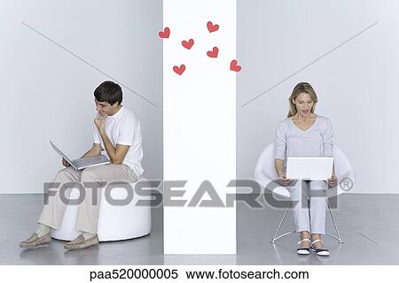 Stock Photography - Man and woman using laptop computers, hearts floating in the air between them. Fotosearch