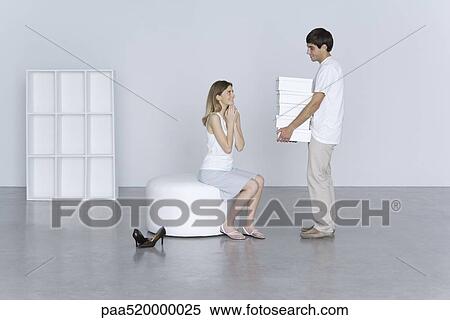 Stock Photography - Man standing before smiling woman, holding large stack of shoe boxes. Fotosearch