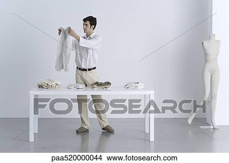 Man standing beside table, holding up sweater View Large Photo Image Picture - Man standing beside table, holding up sweater. Fotosearch