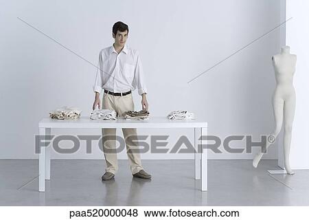 Stock Photo - Man standing beside table with folded clothing, smiling at camera. Fotosearch