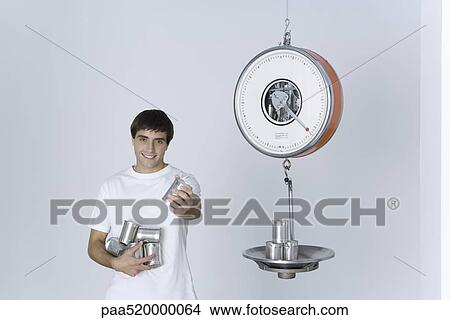 Man weighing cans on scale, offering one can to the camera View Large Photo Image Picture - Man weighing cans on scale, offering one can to the camera. Fotosearch