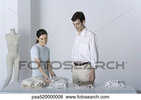 Stock Photo - Saleswoman showing male customer a sweater, both smiling. Fotosearch