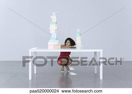 Woman crouching beside table, looking at tall stack of boxes View Large Photo Image Picture - Woman crouching beside table, looking at tall stack of boxes. Fotosearch