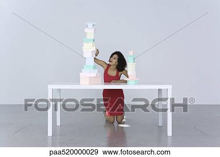 Woman kneeling beside table, looking at tall stack of boxes View Large Photo Image Stock Photo - Woman kneeling beside table, looking at tall stack of boxes. Fotosearch