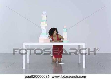 Woman kneeling beside table, looking at stack of boxes View Large Photo Image Stock Photography - Woman kneeling beside table, looking at stack of boxes. Fotosearch