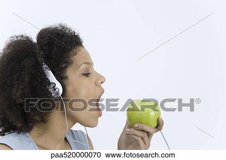 Stock Image - Woman listening to headphones connected to apple, mouth open, profile. Fotosearch