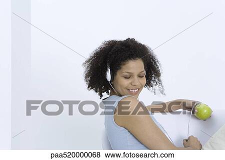 Woman listening to headphones connected to apple, eyes closed View Large Photo Image Stock Photo - Woman listening to headphones connected to apple, eyes closed. Fotosearch