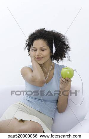 Stock Photograph - Woman listening to headphones connected to apple, eyes closed. Fotosearch