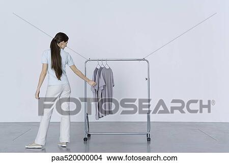 Picture - Woman looking at tee-shirts hanging on rack, rear view. Fotosearch