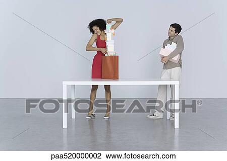 Woman shoving large stack of boxes into shopping bag, man standing nearby with more boxes View Large Photo Image Stock Image - Woman shoving large stack of boxes into shopping bag, man standing nearby with more boxes. Fotosearch