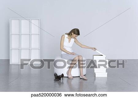 Stock Photograph - Woman sitting beside stack of shoe boxes, peeking in top box. Fotosearch
