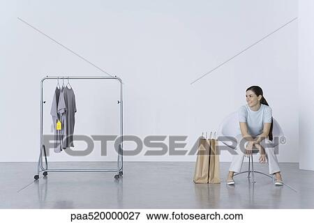 Woman sitting with shopping bags, looking at tee-shirts on nearby rack View Large Photo Image Stock Photo - Woman sitting with shopping bags, looking at tee-shirts on nearby rack. Fotosearch