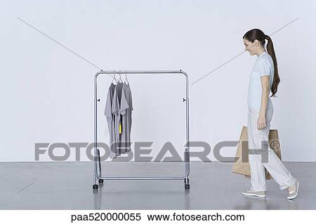 Woman walking toward rack of tee-shirts, carrying shopping bags View Large Photo Image Stock Photography - Woman walking toward rack of tee-shirts, carrying shopping bags. Fotosearch