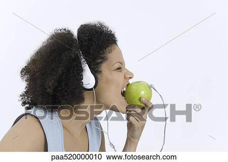 Woman wearing headphones plugged into apple, biting into apple, profile View Large Photo Image Stock Image - Woman wearing headphones plugged into apple, biting into apple, profile. Fotosearch