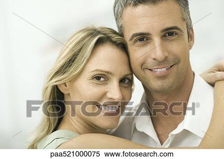 Couple smiling at camera, woman wrapping arms around man, portrait View Large Photo Image Stock Photography - Couple smiling at camera, woman wrapping arms around man, portrait. Fotosearch