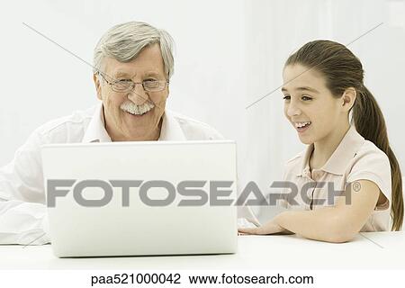 Stock Image - Grandfather and granddaughter looking at laptop together. Fotosearch