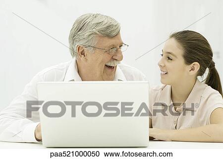 Stock Image - Grandfather and granddaughter sitting with laptop, laughing. Fotosearch