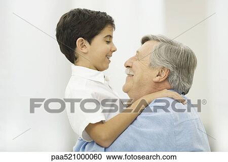 Stock Image - Grandfather holding up grandson, smiling at each other. Fotosearch