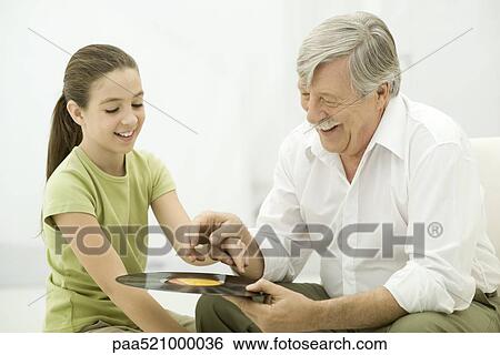 Stock Photograph - Grandfather holding vinyl record, granddaughter pointing. Fotosearch