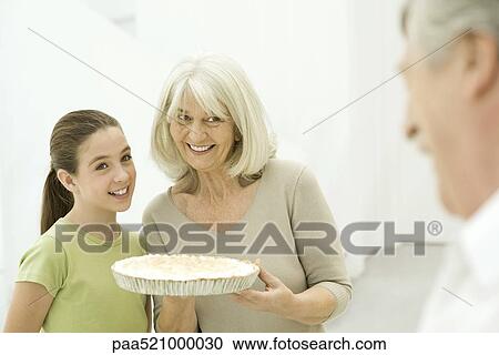 Stock Image - Grandmother and granddaughter side by side, senior woman holding pie. Fotosearch