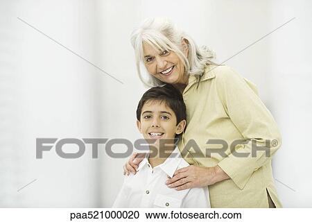 Stock Image - Grandmother standing behind grandson, both smiling at camera, portrait. Fotosearch
