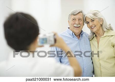 Stock Image - Grandson taking picture of grandparents with digital camera. Fotosearch
