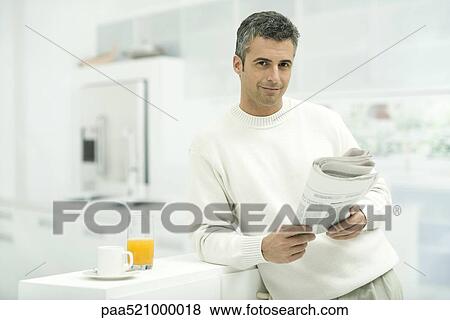 Man leaning against kitchen counter, holding newspaper, smiling at camera View Large Photo Image Stock Photo - Man leaning against kitchen counter, holding newspaper, smiling at camera. Fotosearch