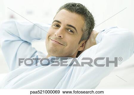 Man leaning back with hands behind head, smiling at camera, portrait View Large Photo Image Stock Photo - Man leaning back with hands behind head, smiling at camera, portrait. Fotosearch