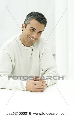 Stock Photograph - Man sitting with hands together, smiling at camera, portrait. Fotosearch