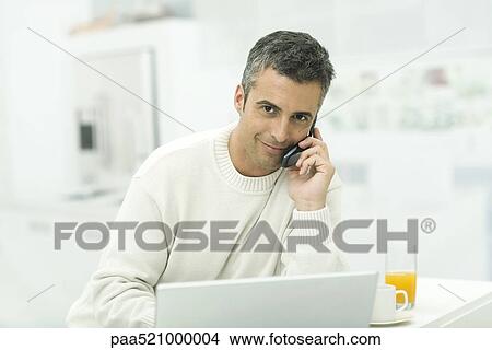 Man talking on cell phone, sitting by laptop and orange juice View Large Photo Image Picture - Man talking on cell phone, sitting by laptop and orange juice. Fotosearch