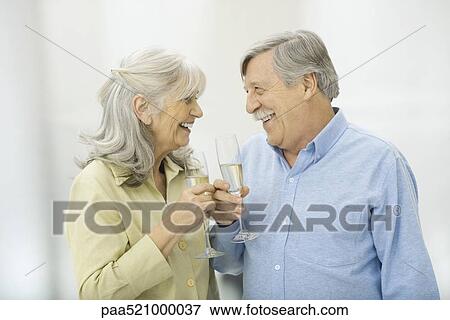 Stock Photo - Senior couple holding champagne flutes, smiling at each other. Fotosearch
