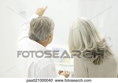 Stock Image - Senior couple looking at floor plans, rear view. Fotosearch