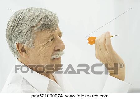 Picture - Senior man holding dart, aiming. Fotosearch