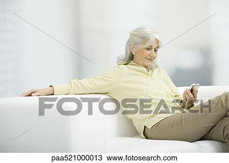 Senior woman listening to MP3 player, sitting on couch View Large Photo Image Stock Image - Senior woman listening to MP3 player, sitting on couch. Fotosearch