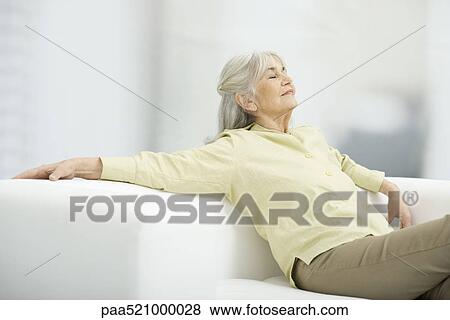 Stock Photo - Senior woman relaxing on couch, eyes closed. Fotosearch