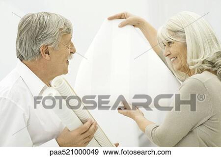 Stock Photo - Senior woman showing wallpaper sample to senior man. Fotosearch