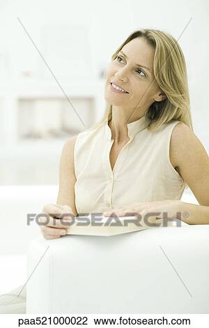 Stock Image - Woman holding closed book, looking away. Fotosearch