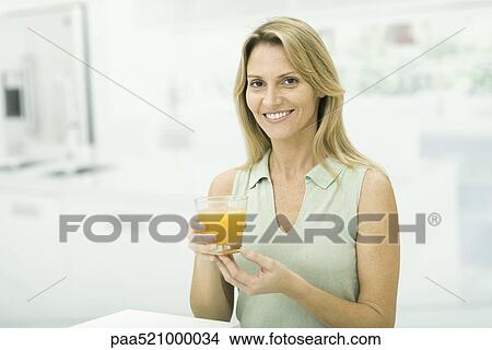 Woman holding up glass of orange juice, smiling at camera, portrait View Large Photo Image Picture - Woman holding up glass of orange juice, smiling at camera, portrait. Fotosearch