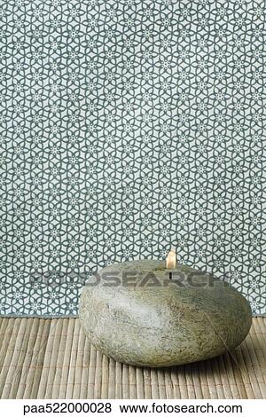 Stock Photo - River rock shaped candle burning. Fotosearch