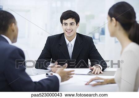 Businessman sitting at desk, talking with clients and smiling View Large Photo Image Stock Image - Businessman sitting at desk, talking with clients and smiling. Fotosearch