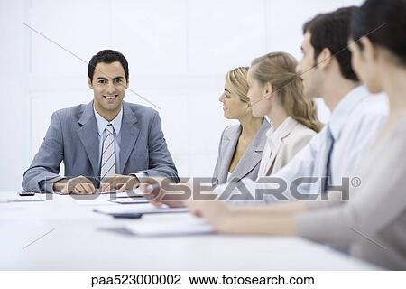 Businessman sitting with colleagues at conference table, smiling at camera View Large Photo Image Stock Image - Businessman sitting with colleagues at conference table, smiling at camera. Fotosearch