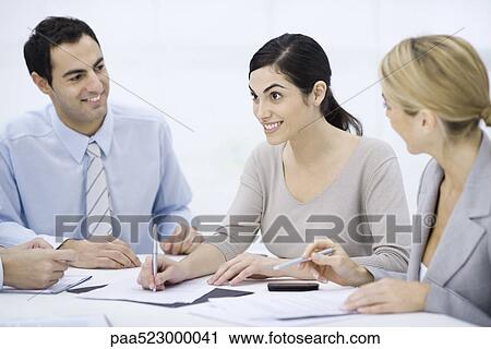 Stock Image - Businessman sitting with colleagues at conference table. Fotosearch