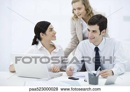 Colleagues gathered around laptop computer, smiling View Large Photo Image Stock Photo - Colleagues gathered around laptop computer, smiling. Fotosearch