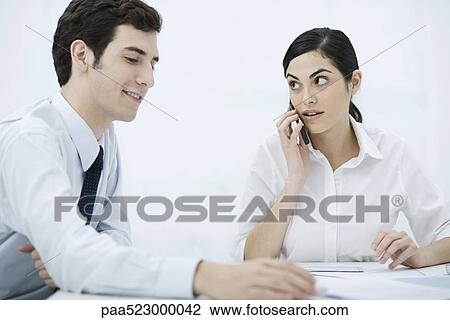 Colleagues sitting together at desk, woman using cell phone View Large Photo Image Stock Image - Colleagues sitting together at desk, woman using cell phone. Fotosearch