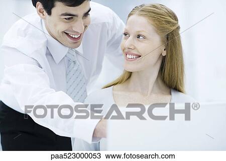 Professional man leaning over female colleague's shoulder, pointing at laptop, woman smiling at him View Large Photo Image Stock Image - Professional man leaning over female colleague's shoulder, pointing at laptop, woman smiling at him. Fotosearch