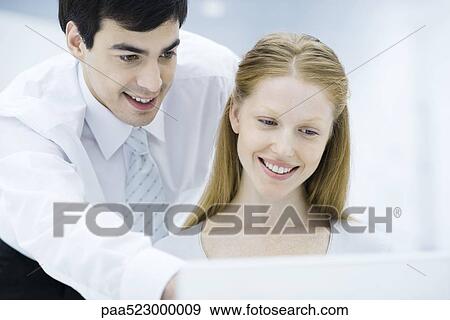 Professional man looking over female colleague's shoulder, pointing at laptop computer View Large Photo Image Stock Photo - Professional man looking over female colleague's shoulder, pointing at laptop computer. Fotosearch
