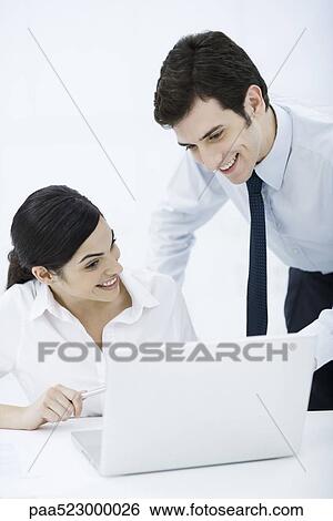 Professional man looking over female colleague's shoulder at laptop computer, both smiling View Large Photo Image Stock Photograph - Professional man looking over female colleague's shoulder at laptop computer, both smiling. Fotosearch
