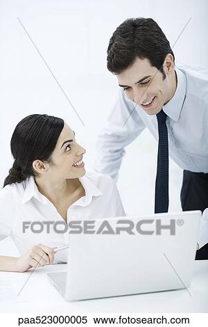 Professional woman sitting with laptop, male colleague looking over her shoulder, both smiling View Large Photo Image Stock Photography - Professional woman sitting with laptop, male colleague looking over her shoulder, both smiling. Fotosearch