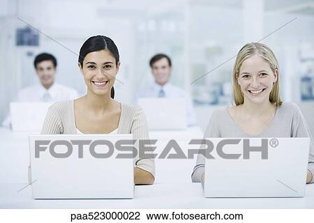 Professional women using laptop computers, smiling at camera, colleagues in background View Large Photo Image Stock Image - Professional women using laptop computers, smiling at camera, colleagues in background. Fotosearch
